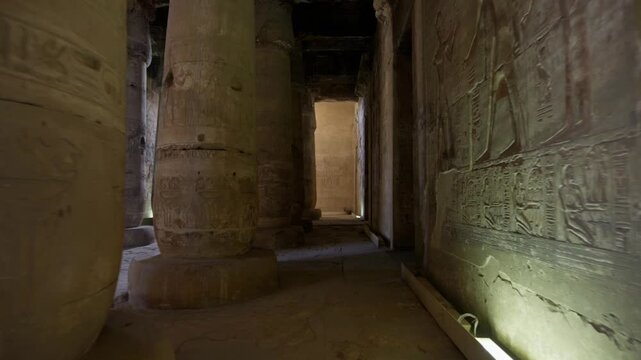 Dramatic interior of Abydos temple, Upper Egypt, with rows of colossal columns bearing hieroglyphic inscriptions, relief carvings and faded ceiling paintings in moody light.