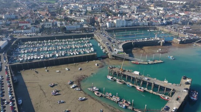 St Peter Port Guernsey very high reveal of Albert and Victoria marinas divided by Albert Pier with town spread out behind and boats dreid out in fisherman&rsquo;s marina in golden hour sun at low tide.