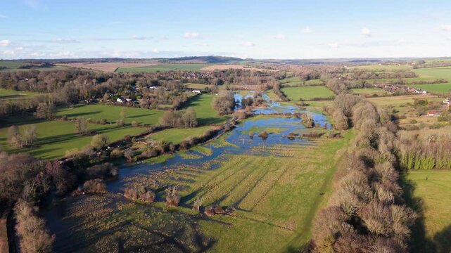 Reveal drone footage following the river pulling back over flooded fields in glorious English countryside in the Southdowns National Park in afternoon sun with extensive views to distant hills