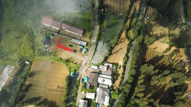4K Aerial view of outdoor event setup and agricultural farm terraces in a misty mountain village.