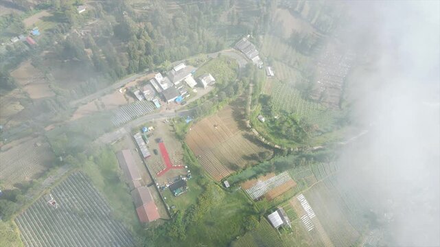 4K Aerial view of outdoor event setup and agricultural farm terraces in a misty mountain village.