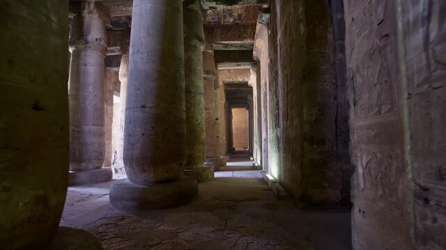Looking down a dimly lit colonnade of carved stone columns inside the great temple of Abydos, Seti I, Egypt, walls covered in hieroglyphic reliefs and painted scenes.