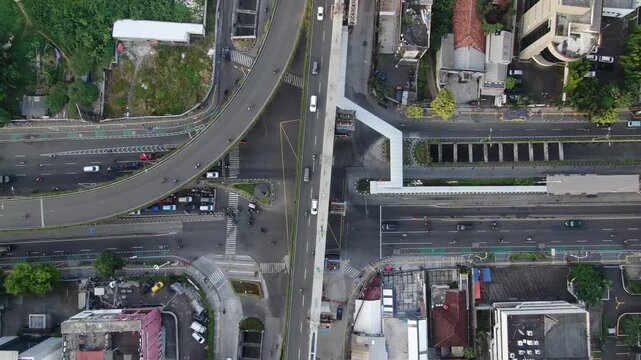 Jakarta, Indonesia - April 26th 2026: Aerial Top-down View of Busy City Intersection with Curved Flyover and Elevated Rail Construction. Urban Infrastructure under Hazy Overcast Sky