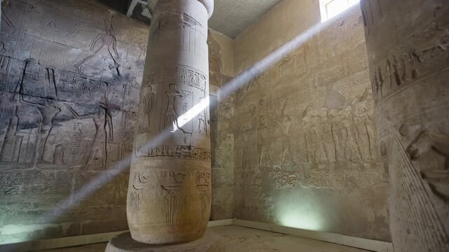 Ethereal shaft of sunlight piercing the dark interior of Abydos hypostyle hall, Egypt, between colossal ancient columns with carved reliefs on cracked stone floor.