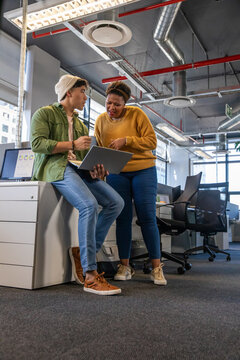 Diverse coworkers collaborating around laptop in modern open-plan office, pointing at monitor