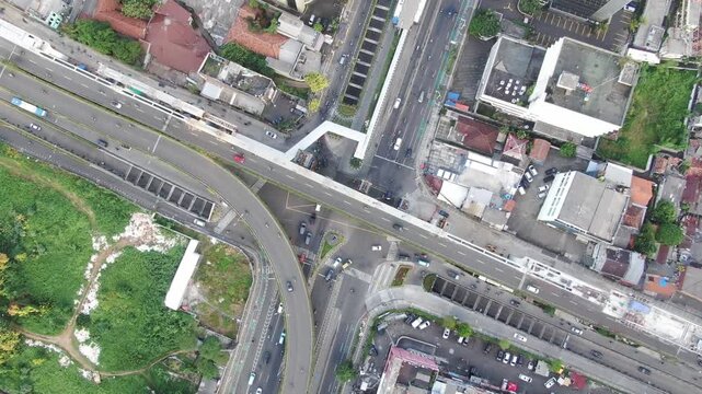 Jakarta, Indonesia - April 26th 2026: Aerial Top-down View of Busy City Intersection with Busway, Curved Flyover, and Elevated Rail Construction. Urban Infrastructure under Hazy Overcast Sky