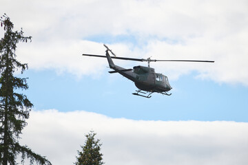 Fototapeta premium Military Helicopter In Flight Over Forest Trees Against Blue Sky During Daytime Training