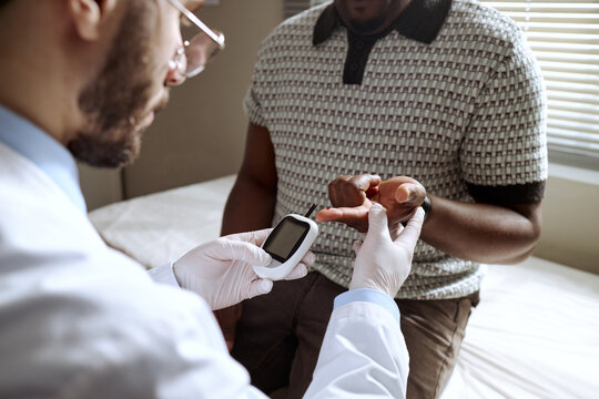 Close up of Caucasian male doctor checking blood sugar of Black middle aged man with glucometer during exam. Useful for diabetes care, screening, treatment marketing