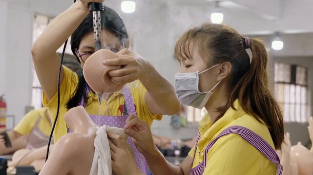 Two female workers carefully cleaning and finishing a silicone doll torso on a factory production line