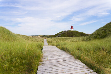 Naklejka premium Wide shot of a wooden path on dunes to a small lighthouse | Amrum, Germany 
