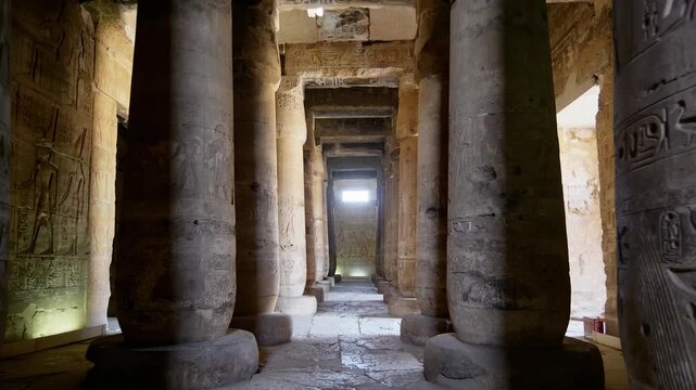 Grand colonnaded hall inside Abydos temple dedicated to Seti I, Egypt, with towering carved columns, relief-covered walls and atmospheric golden illumination from below.