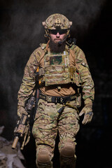 Obraz premium Armed Soldier in Tactical Gear Walking Through Dust With Rifle and Ballistic Helmet