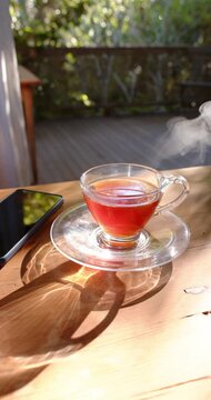 Vertical video: Glass cup and saucer on deck releasing steam as sun warming tea and camera tilting