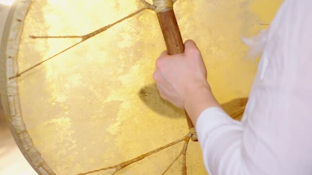 Close up of a hand gripping the handle of a large frame drum, with warm light revealing natural skin texture and lacing. Drum meditation supports grounding, stress relief, and mindful focus.