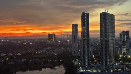 Fototapeta premium Dramatic golden sunset over a modern city skyline with tall skyscrapers and urban residential area.