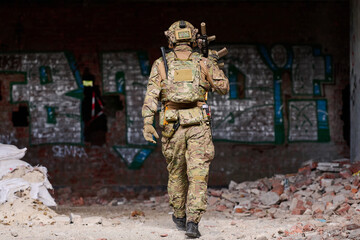 Obraz premium Soldier in Camouflage Tactical Gear Walking Through Abandoned Graffiti-Covered Building During Urban Military Training