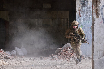 Obraz premium Armed Soldier In Camouflage Running Through Dusty Urban Ruins During Tactical Combat Training Operation