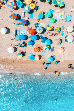 Aerial view of colorful umbrellas on sandy beach, swimming people in blue sea on sunny summer day. Sardinia, Italy. Tropical landscape with clear turquoise water. Travel and vacation. Top down view