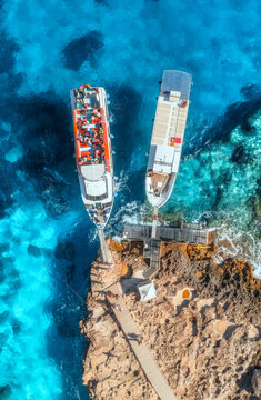 Aerial view of boat with people and rocky sea coast on sunny summer day. Top drone view of yacht, transparent azure water, path. Mediterranean sea. Travel in Sardinia island, Italy. Tropical landscape