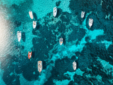 Aeria drone view of boats floating in shallow turquoise sea above rocky seabed with sunlight reflections, calm summer scene near Mallorca, Balearic Islands, Spain. Colorful seascape. Top down view