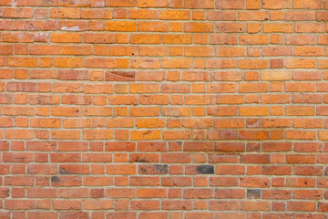 Fototapeta premium This high-resolution photograph features a weathered orange and red brick wall with a rustic texture, showcasing a traditional masonry pattern and aged mortar joints.