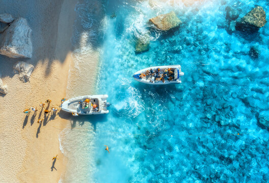 Aerial view of boats, sandy beach and blue sea with waves at sunset. Summer in Sardinia, Italy. Top drone view of motorboats, shore, stones in transparent water. Colorful tropical landscape. Travel