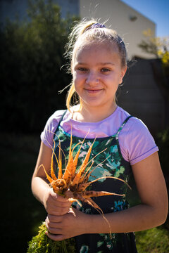 Girl holding freshly harvested carrot in home garden