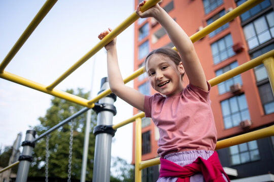 happy child playing on playground outdoor. girl doing sports on playground in yard of multi-storey building in summer