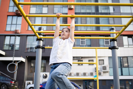 happy child playing on playground outdoor. girl doing sports on playground in yard of multi-storey building in summer