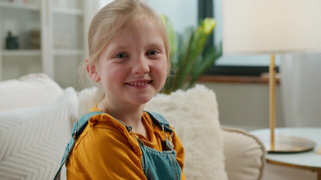 Happy headshot of Caucasian little 5s cute girl smiling toothy looking at camera child blonde kid daughter smile satisfied funny good mood emotion posing at home couch sofa enjoy childhood custody