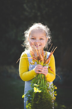 Young girl holding freshly harvested vegetables outdoors