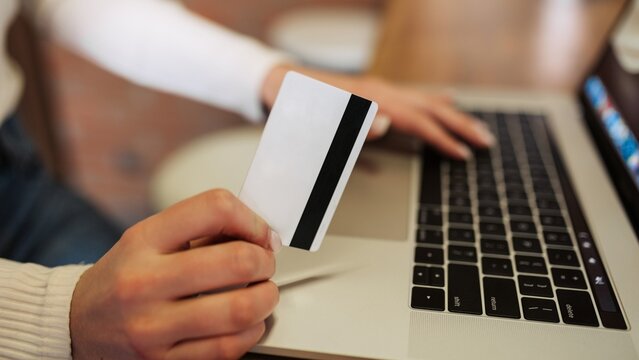 Person holding credit card while making secure online payment on laptop for e-commerce purchase