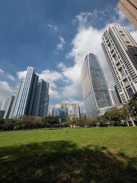 Vibrant modern cityscape of Bonifacio Global City, Manila, showcasing impressive skyscrapers towering over a serene expanse of verdant parkland under a bright, partly cloudy day. Urban architecture