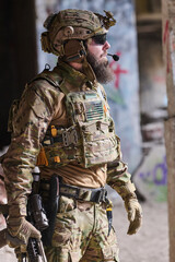 Obraz premium Bearded Soldier in Tactical Gear With Helmet and Rifle in Urban Military Training Environment