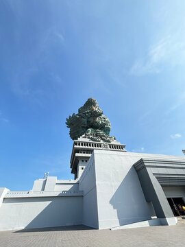Wide angle view of the majestic Garuda Wisnu Kencana (GWK) statue and its massive pedestal building in Bali under a clear blue sky.