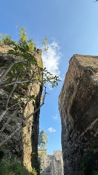 The majestic Garuda Wisnu Kencana statue viewed between two towering limestone cliffs under a clear blue sky in Bali.