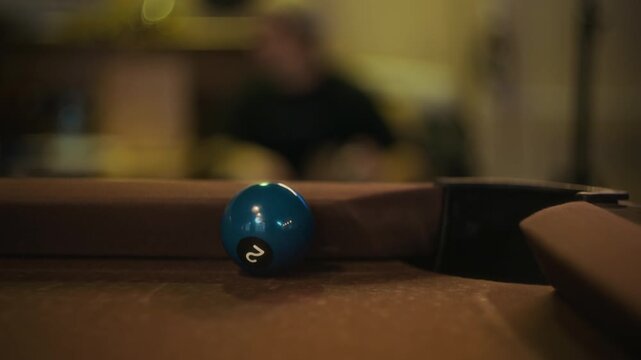 Extreme close up of billiard ball sinking into pocket after precise shot during match on brown felt table at pool hall, slow motion