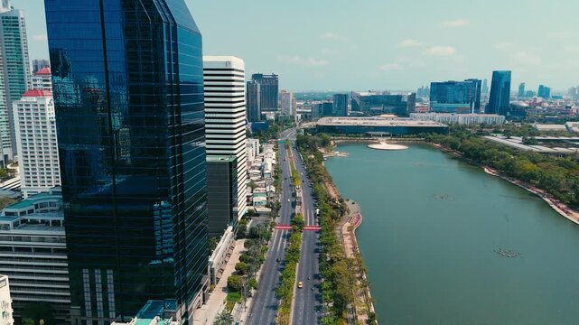 Aerial drone view of Ratchadaphisek Road beside Benjakitti Park lake showing modern towers Queen Sirikit National Convention Center and Sukhumvit skyline with urban traffic and greenery