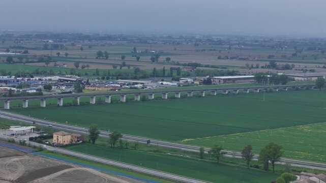 Railway viaduct near Fiorenzuola d Arda PC Emilia Romagna Italy along Milano Bologna railway parallel to Autostrada A1 and service area within Pianura Padana farmland, drone lateral pan right