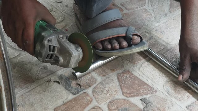Closeup of a laborer using an electric angle grinder to cut a metal pipe on a tiled floor, creating bright sparks. Ideal for construction and industrial safety content.