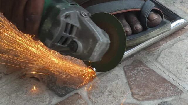 Close up of an Indian laborers hand using a power tool to cut a metal pipe, creating bright orange sparks. Ideal for construction, DIY, and industrial safety content.