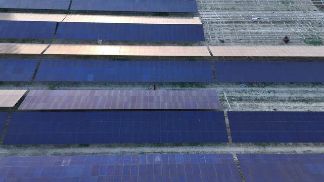Solar panel arrays seen from a top down perspective forming parallel lines across a flat installation site within a rural energy facility, emphasizing geometry and land use organization, drone shot