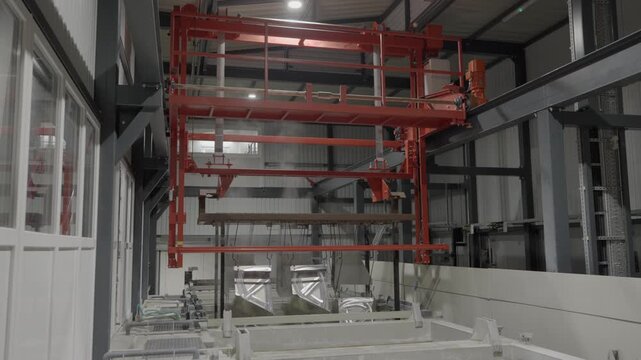 Metal sheets are being lifted out of a hot coating bath during the KTL coating (cathodic dip coating) process in an industrial factory. As the parts emerge from the liquid, visible steam rises from th