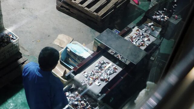 High angle view of a food production line with a worker sorting candy moving on a conveyor belt