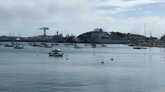 Tranquil wide angle view over the River Fal at Falmouth, Cornwall, with the imposing RFA Argus docked in background, scattered leisure boats, calm water, and overcast skies. No people visible.