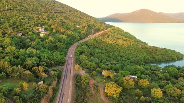 Aerial view of car driving on mountain road by lake at sunset, scenic landscape travel and freedom concept in nature