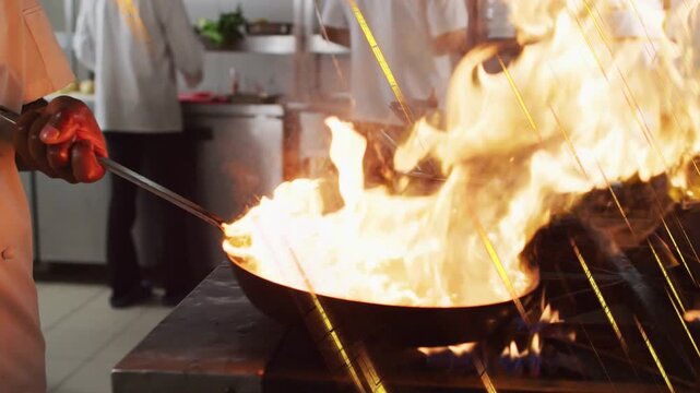 Chef stirring pan on gas range in kitchen, flame bursting over rim, tilting pan controlling flare