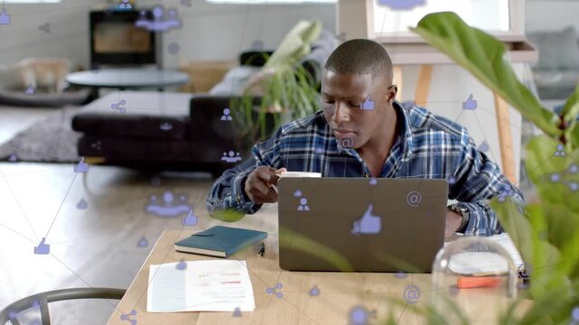 Man working remote glancing at laptop reaching mug, sipping for focus while purple icons floating