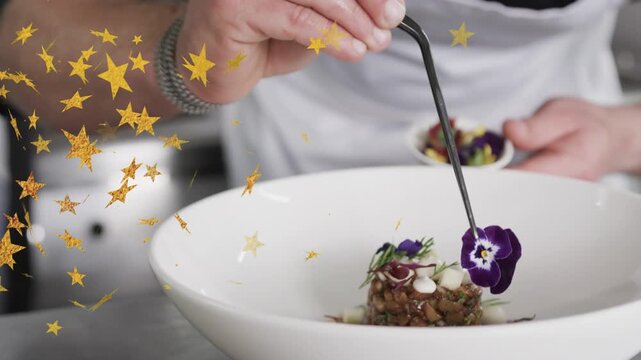 Male chef picking pansy from ramekin placing garnish on dish for plating, gold star overlaying left