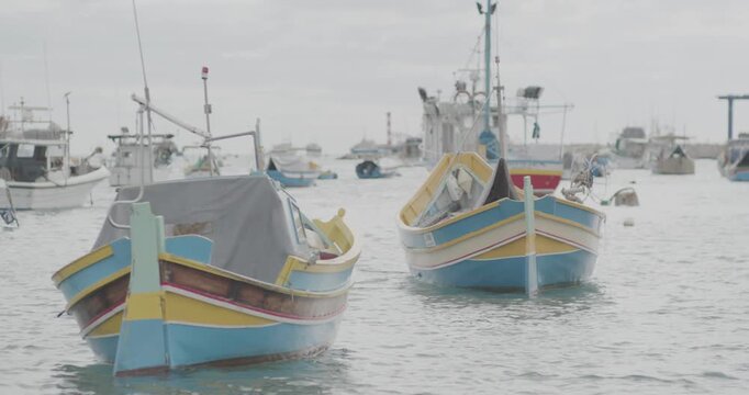 Traditional colorful Luzzu fishing boats moored in a calm harbor on a cloudy day